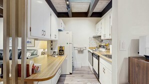 Eine schmale Küche mit weißen Schränken, einer Holz Arbeitsplatte und einer gefliesten Spritzschutzwand.