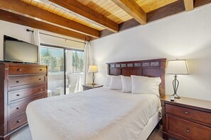 Ein Schlafzimmer mit Holzboden, einem Bett mit weißer Bettwäsche, einem Schminktisch, einem Nachttisch mit Lampen und einem Fernseher auf dem Schminktisch.