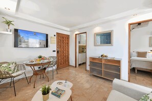 Ein Wohnzimmer mit Fernseher, Esstisch, Stühlen, einer Couch, einem Konsolentisch und einem Bett.