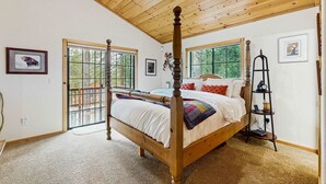A bedroom with a four-poster bed, a wooden ceiling, and a view through a sliding glass door. - Charming mountain home with game room, decks, and stunning views (Truckee)