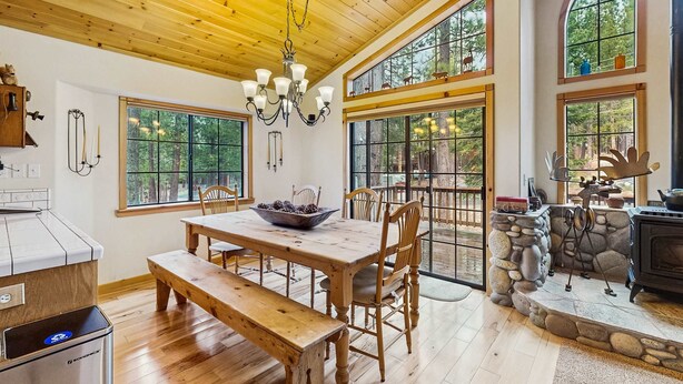 A wooden dining table with chairs, a chandelier, and a stone fireplace. - Charming mountain home with game room, decks, and stunning views (Truckee)