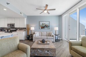 A spacious living area with a kitchen, a ceiling fan, a dining table, and a large window. - Lighthouse 1615 by Liquid Life (Gulf Shores)