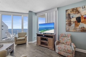 Una sala de estar con televisor, un sofá, una silla y un balcón con vistas al océano.