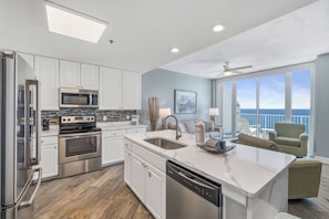 A modern kitchen with stainless steel appliances, a dishwasher, and a large island with a sink. - Lighthouse 1615 by Liquid Life (Gulf Shores)