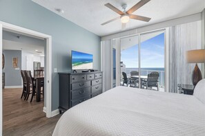Una camera da letto con un letto grande, un ventilatore a soffitto, un televisore su un comò e un balcone con vista sull'oceano.