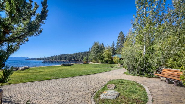 A paved pathway leading to a bench, a grassy area, and a view of a body of water with trees and a distant shoreline. - Homey Family Condo with Shared Pool, Hot Tub, Tennis & Lovely Lake Views (Tahoe City)