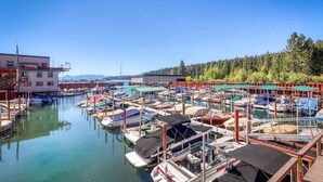 A marina with boats docked, a building with a red roof, and a forested hillside in the background. - Homey Family Condo with Shared Pool, Hot Tub, Tennis & Lovely Lake Views (Tahoe City)