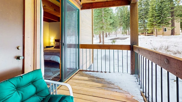 A wooden deck with a green chair, a sliding glass door leading to a room, and a view of snow-covered ground and trees. - Cozy townhouse with pool access, board games, and fireplace - near skiing (Northstar - Truckee)