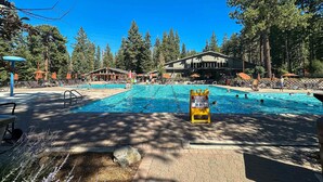 A swimming pool with a lifeguard sign, surrounded by lounge chairs and umbrellas, with a building in the background. - Cozy townhouse with pool access, board games, and fireplace - near skiing (Northstar - Truckee)