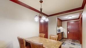 A dining area with a wooden table and chairs, a chandelier, and a kitchen in the background. - Everline Resort & Spa Ski-in-ski-out condo, pools, tennis, ice rink, & gym (Olympic Valley)