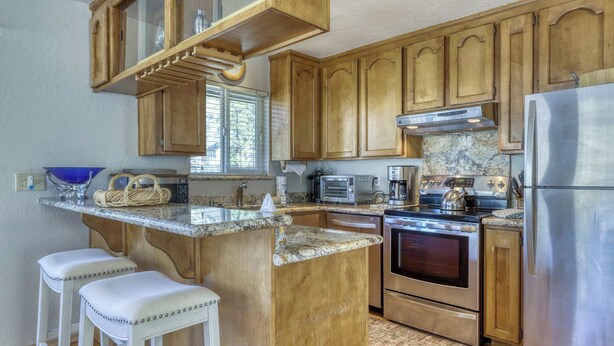Cucina con mobili in legno, frigorifero in acciaio inossidabile, forno integrato e piano di lavoro in granito.