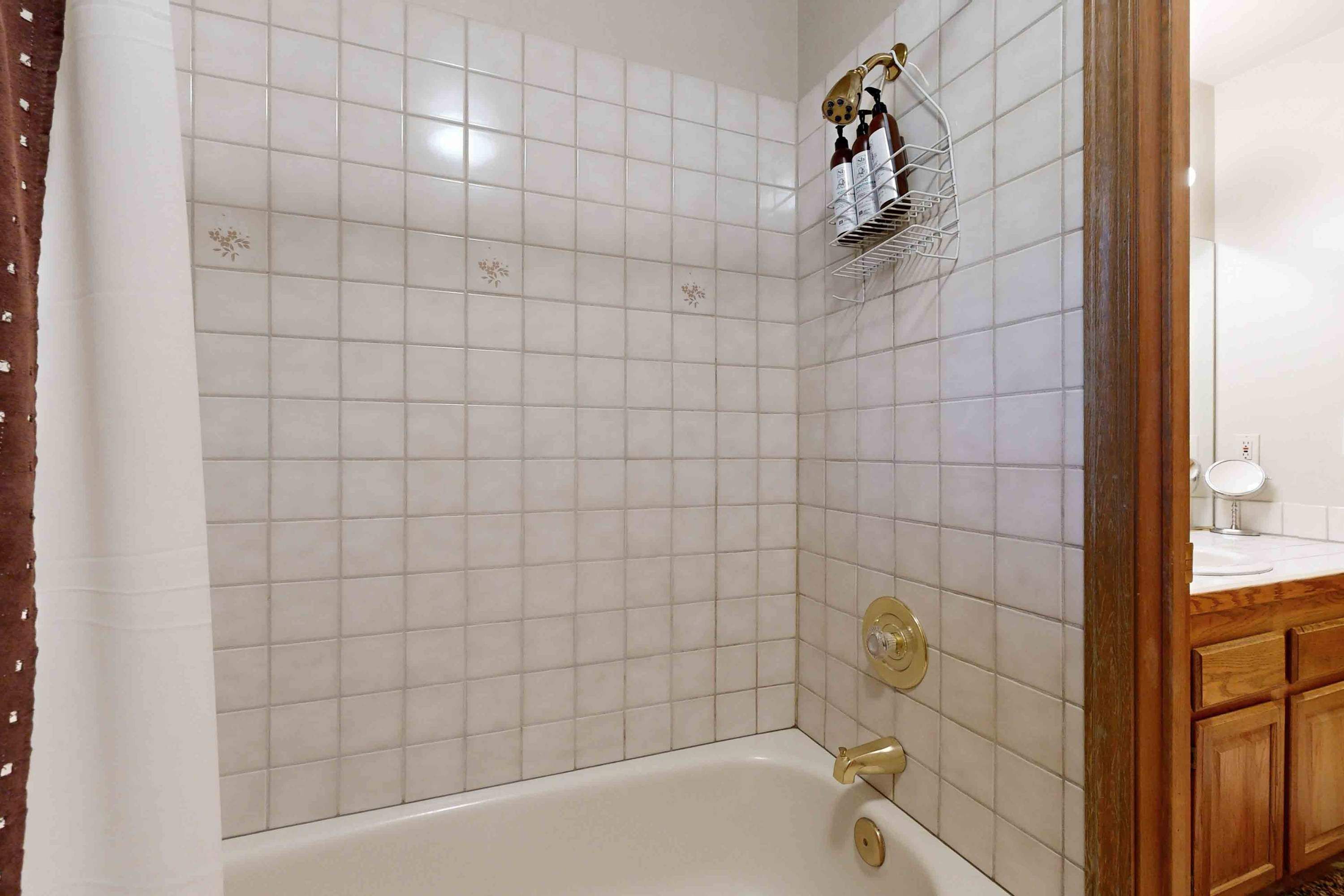 A bathroom with white tiled walls, a bathtub, a shower area, and wooden cabinets.