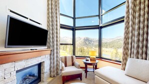 Ein modernes Wohnzimmer mit Kamin aus Stein, einem Flachbildfernseher, einer bequemen Couch, einem kleinen runden Tisch und einem großen Fenster mit Bergblick.