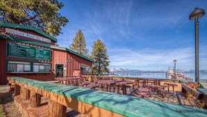 Eine Holzterrasse mit Tischen, Bänken, einer Speisekarte und Blick auf das Wasser und die Berge.