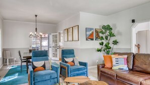 Ein Wohnzimmer mit blauem Sessel, braunem Ledersofa, Couchtisch aus Holz und einer Deckenleuchte.