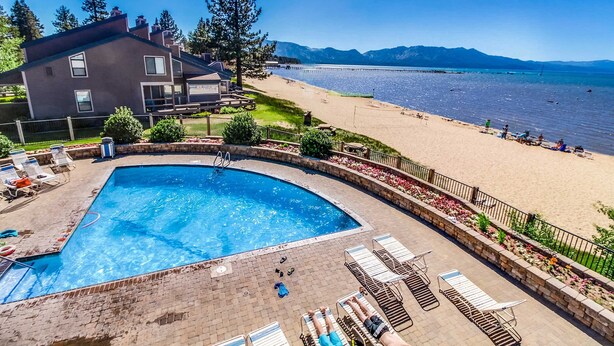 Ett poolområde med solstolar, en swimmingpool och utsikt över stranden och bergen.