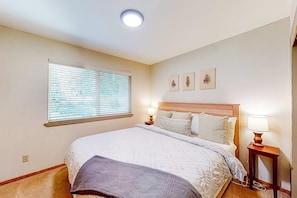 Une chambre à coucher avec un lit, une fenêtre avec des stores, une table de chevet avec une lampe et des œuvres d’art murales.