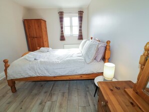 A bedroom with a wooden bed, a nightstand, a wooden wardrobe, and a window with curtains. - Innishore Cottage (Enniskillen)