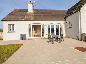 A house with a patio, a sliding glass door, and a small table with chairs. - Innishore Cottage (Enniskillen)