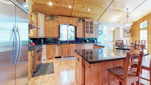 Una cocina con armarios de madera, un refrigerador de acero inoxidable, una isla central y una zona de comedor con sillas.