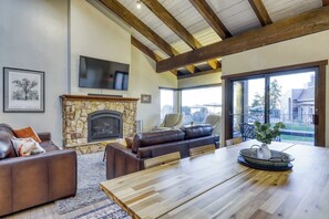 Una sala de estar con chimenea de piedra, sofás de cuero, una mesa de comedor y un televisor montado en la pared.