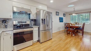 A modern kitchen with stainless steel appliances, a dining area with wooden furniture, and a window providing natural light. - Dog-Friendly Getaway | Deck, Sauna, Grill, Foosball, Parks & Trails (South Lake Tahoe)