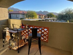 Ein Balkon mit Tisch, Stühlen und Flaschen, mit Blick auf eine Wohngegend mit Häusern und Bergen.