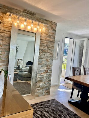Un intérieur moderne avec un mur en pierre, un coin repas et une vue à travers une porte vitrée.