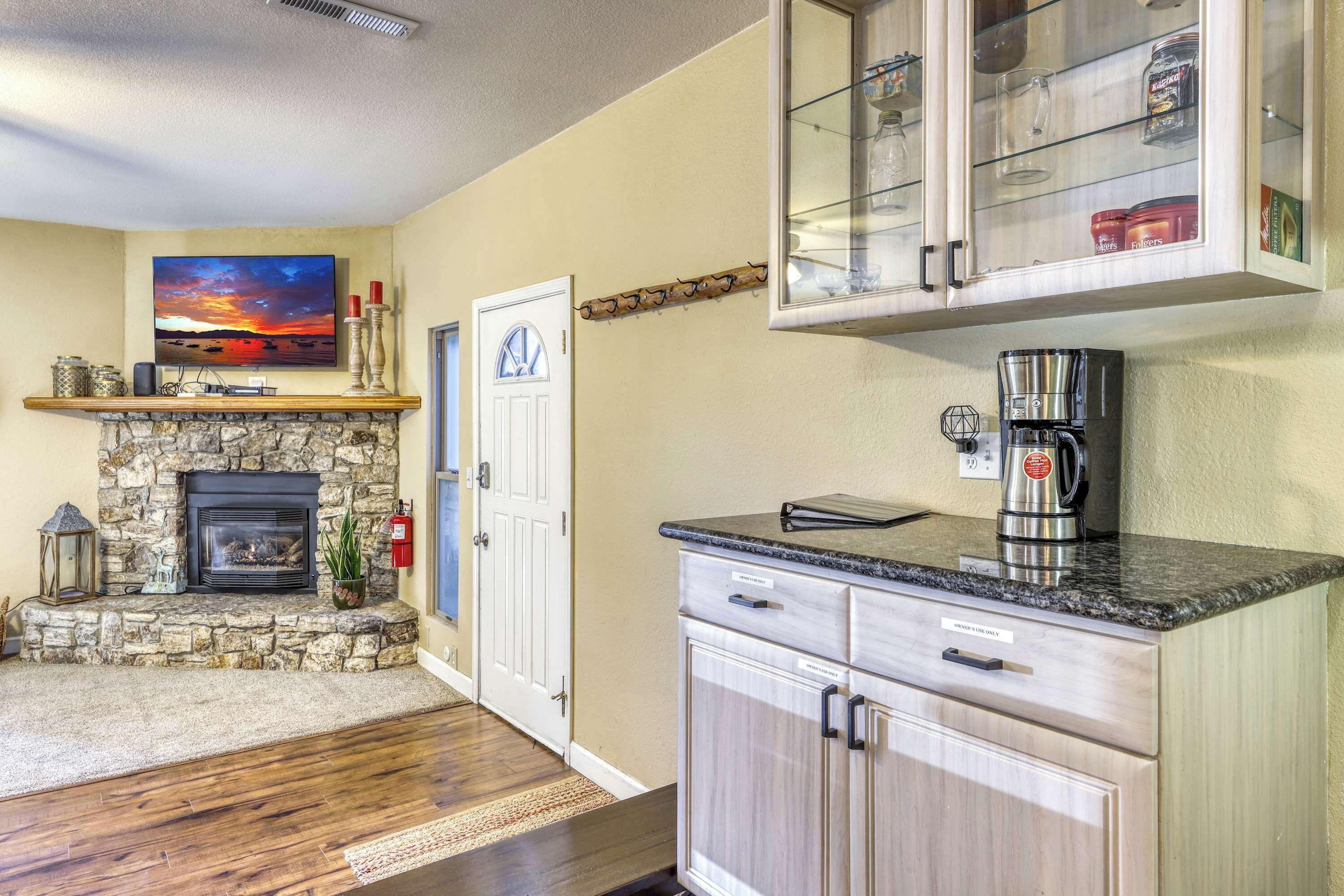 A living room with a stone fireplace, a television, and a kitchen area with a coffee maker.