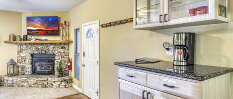 A living room with a stone fireplace, a television, and a kitchen area with a coffee maker.