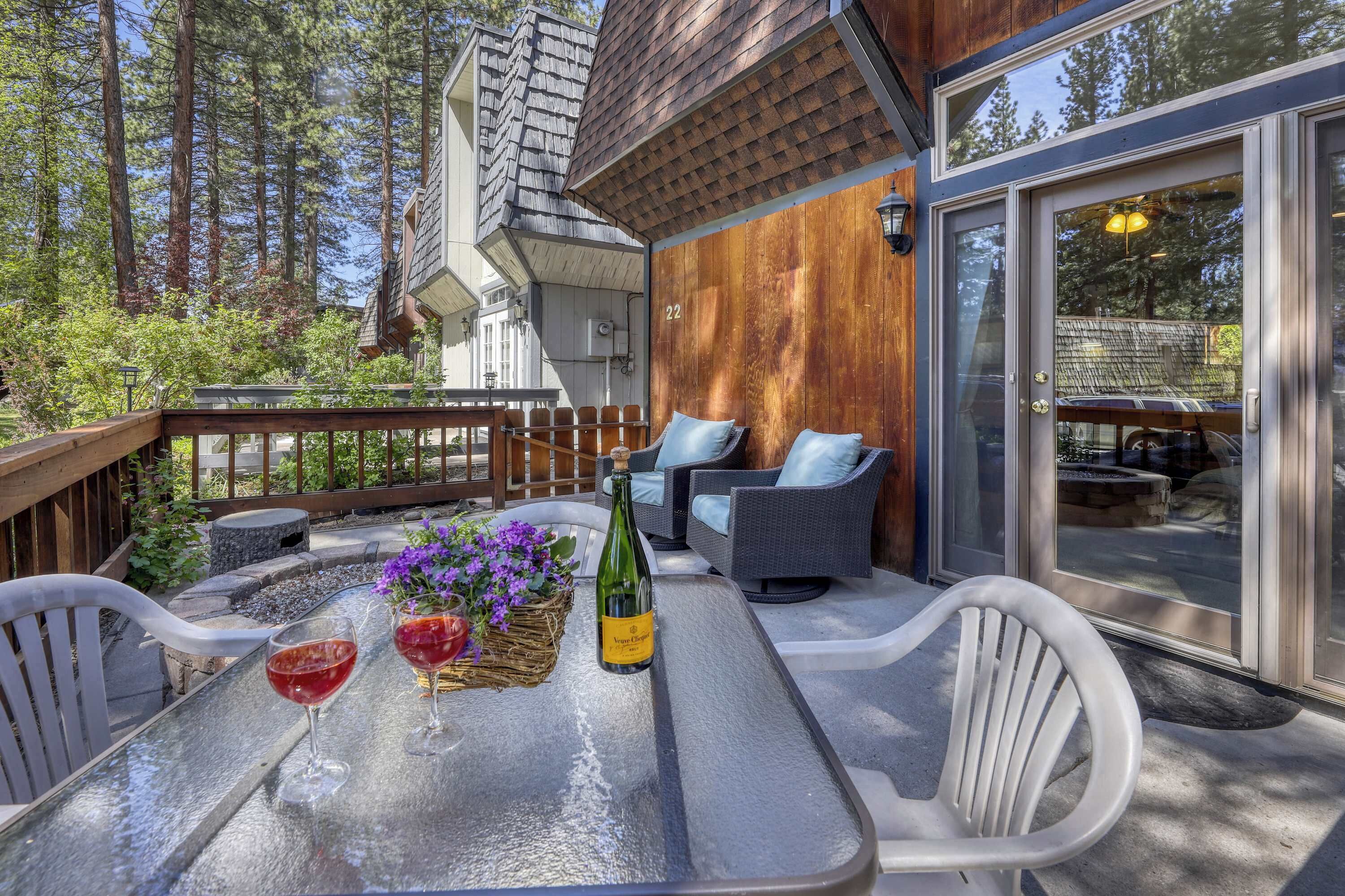 An outdoor patio with a table, chairs, and a bottle of wine.