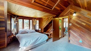 A wooden room with a bed, nightstands, and a door leading to another room. - Riverfront dog-friendly retreat with a rustic flair & wood stove, near skiing (Soda Springs)