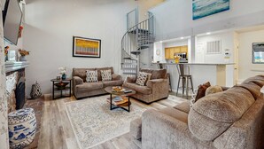 Ein geräumiges Wohnzimmer mit Kamin, Sofas, einem Couchtisch und einer Wendeltreppe, die in eine obere Etage führt.