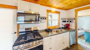 Une cuisine équipée d’une cuisinière, d’un four à micro-ondes et d’un évier, avec un plafond en bois et des armoires blanches.
