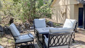 Une terrasse aménagée avec du mobilier d’extérieur, comprenant une table et deux chaises, le tout mis en valeur par un bâtiment en arrière-plan et une végétation naturelle.