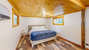 Une chambre avec un plafond en bois, un lit recouvert d’une couverture bleue et une petite table avec une lampe.