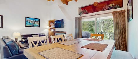 Un comedor con una mesa de madera, sillas y un televisor en la pared.