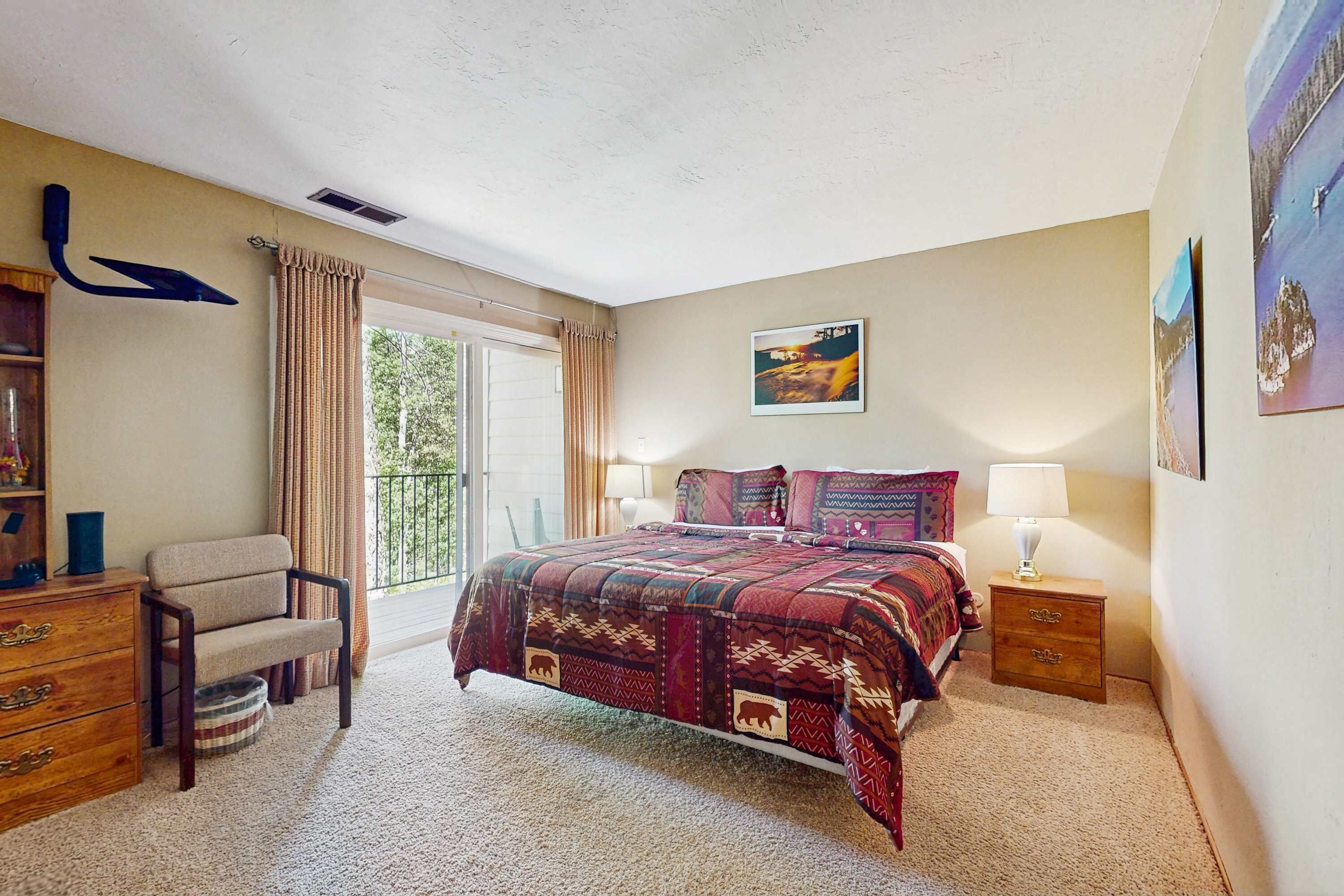 A bedroom with a bed, a chair, a nightstand, a lamp, a window with curtains, and a painting on the wall.