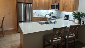 Una cocina moderna con armarios de madera, electrodomésticos de acero inoxidable, una isla central con taburetes y un microondas sobre el fregadero.