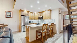 Una cocina moderna con armarios de madera, electrodomésticos de acero inoxidable y una isla central con taburetes de bar.