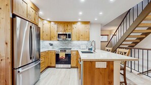 Una cocina moderna con armarios de madera, electrodomésticos de acero inoxidable, una isla central y una escalera.