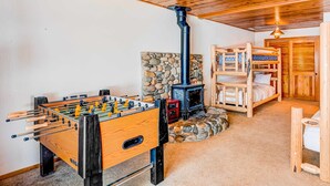 A cozy room with a foosball table, a stone wall, a wood-burning stove, and a bunk bed. - Fun home with foosball table - near on-site golf, pools & hot tub (NorthStar-Truckee)