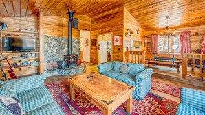 A log cabin interior with a stone fireplace, wooden furniture, and a television. - Fun home with foosball table - near on-site golf, pools & hot tub (NorthStar-Truckee)