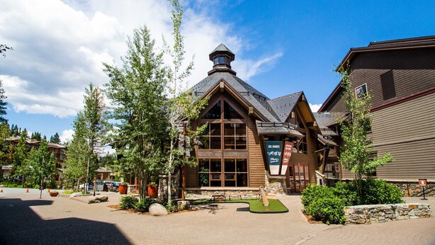 A lodge with a prominent tower, large windows, and a well-maintained outdoor area with trees and a stone pathway. - Fun home with foosball table - near on-site golf, pools & hot tub (NorthStar-Truckee)