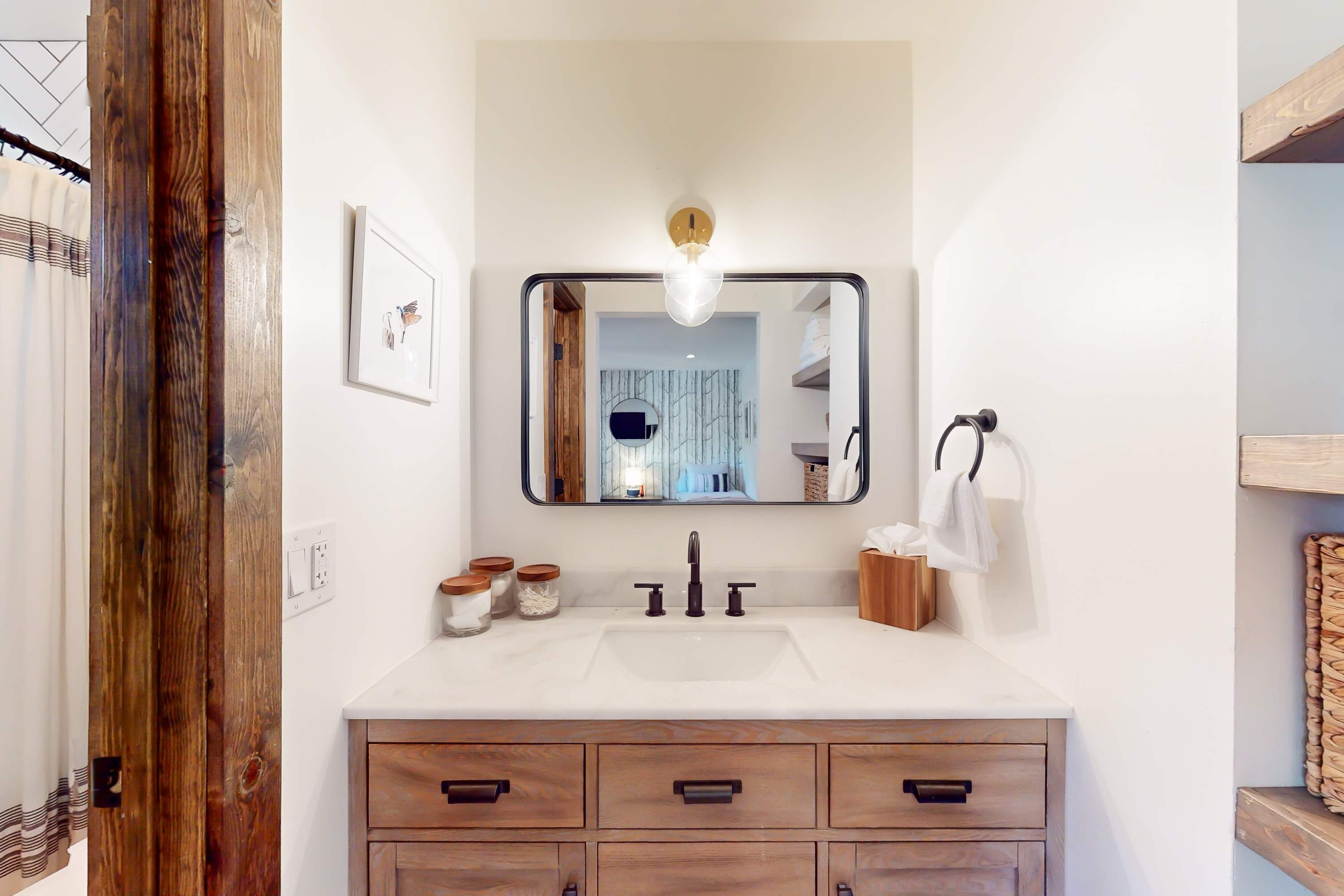 A bathroom with a white sink, wooden vanity, and a mirror with a light fixture.