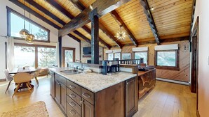 Une cuisine spacieuse dotée d’un grand îlot central, de poutres en bois et de grandes fenêtres.
