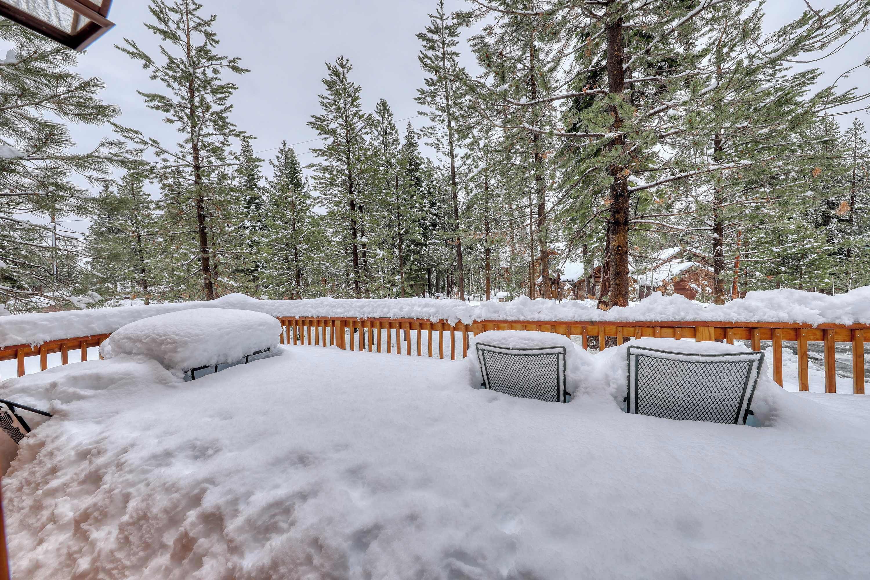 Un espacio al aire libre cubierto de nieve, con una valla de madera, una silla de metal y una mesa semienterrada bajo la nieve.