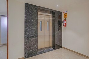 Un pasillo con pared de mármol, puerta de ascensor de vidrio, extintor y letrero de no fumar.