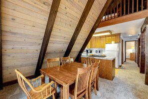 Een eetgedeelte met een houten tafel en stoelen, een keuken op de achtergrond en een slaapverdieping.