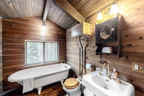 Een houten badhok met bad, toilet, wastafel en spiegel.
